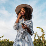 Young woman in a straw hat walking in a path in the middle of a vineyard with a bunch of grapes in hands