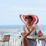 African American woman (30s) enjoying drink at restaurant overlooking beach.