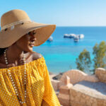 Portrait of beautiful African American model girl in stylish sun hat. Fashion black woman on natural background coast of sea. High quality photo